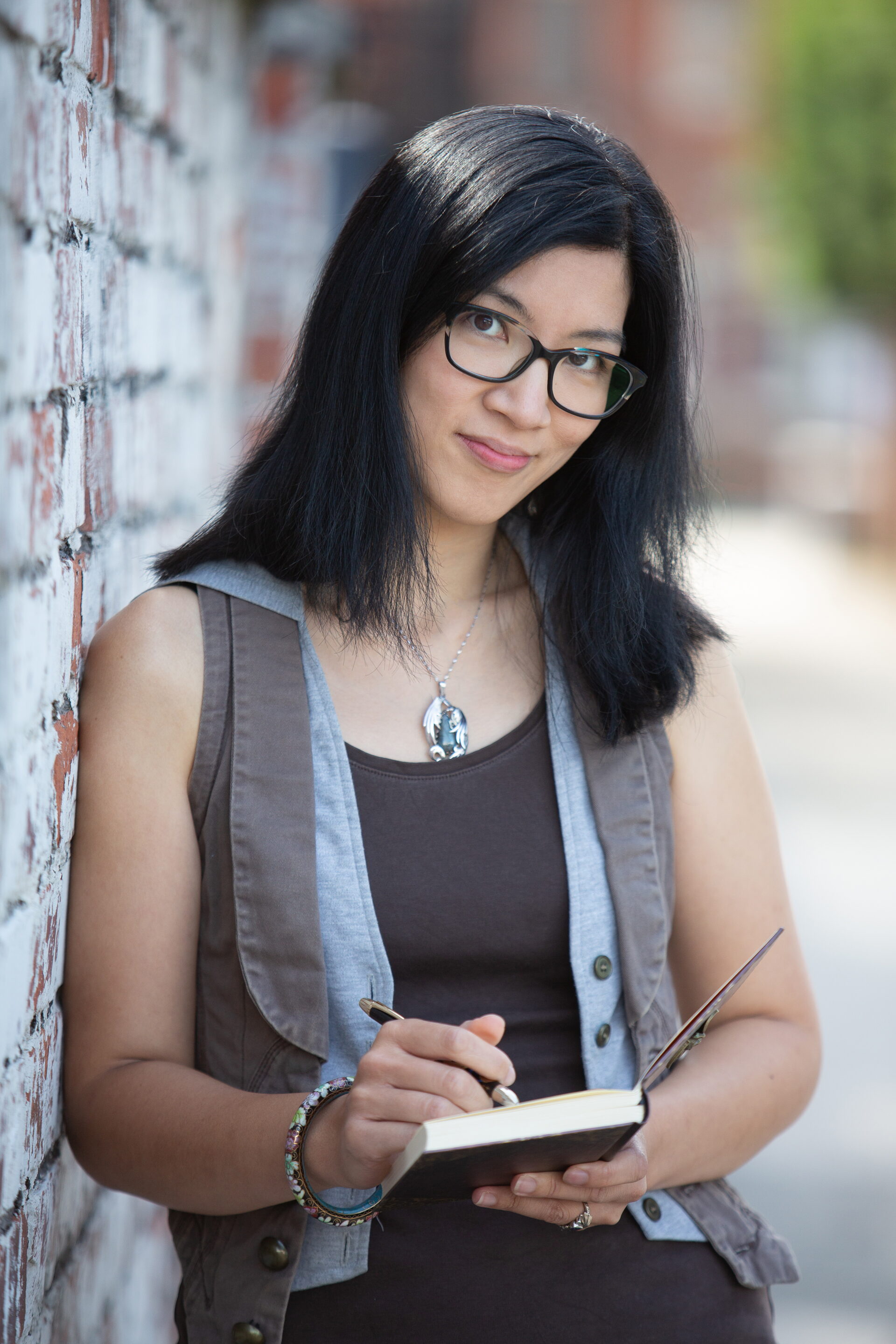 An author photo of Eliza Chan, she is holding a notebook and looking into the camera. Photo by Sandi Hodkinson