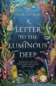 Cover of A Letter to the Luminous Deep by Sylvie Cathrall. The cover shows sunlight filtering through water, with brightly coloured coral bordering the title, as well as old books and a fountain pen nestled on the ocean floor.