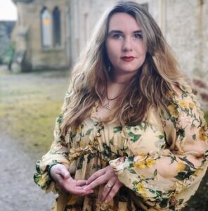 A photo of S.T. Gibson in a floral dress, standing near some gothic ruins